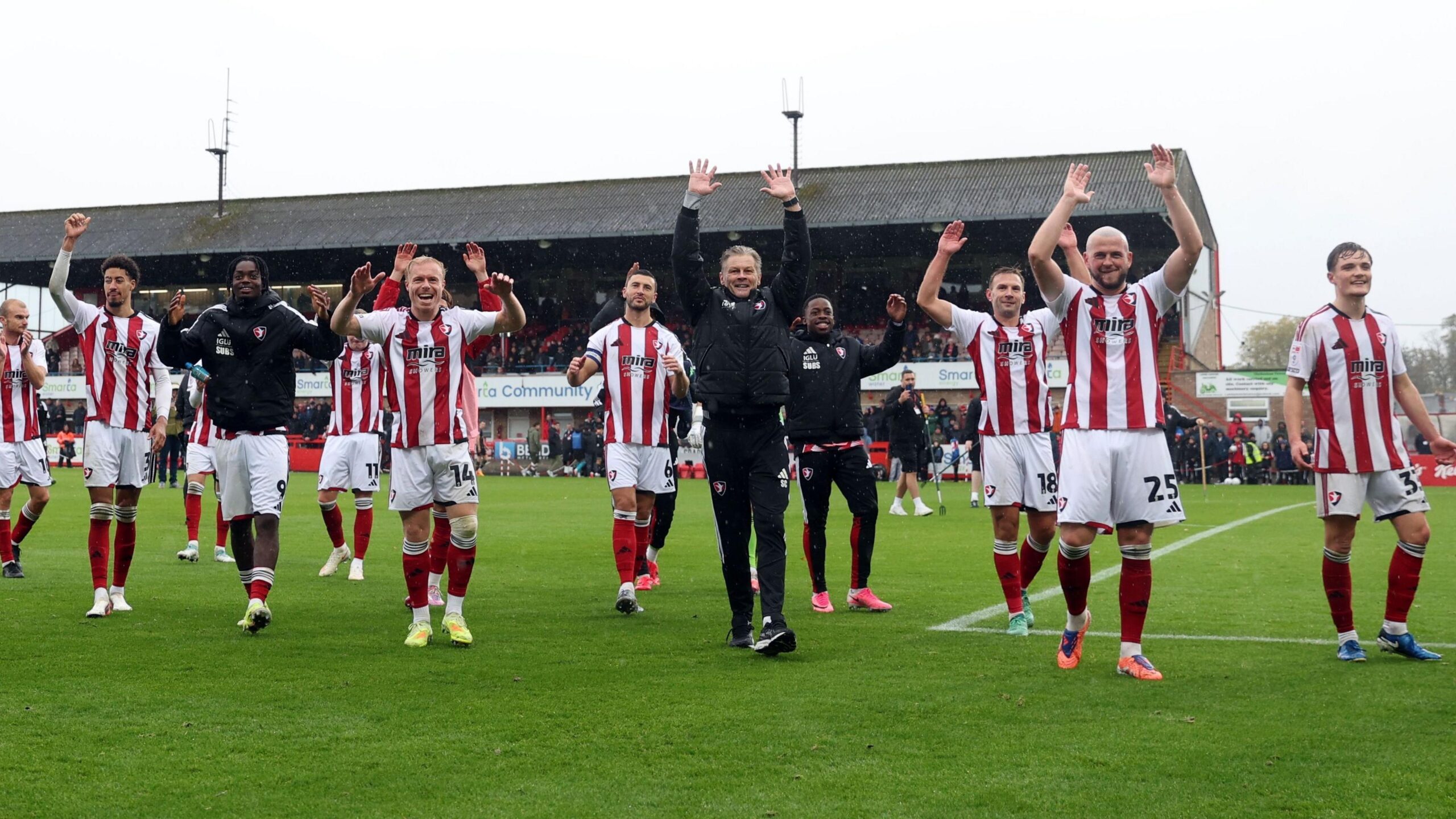 Cheltenham Town players and staff celebrate after their win over Newport. Steve Cotterill is in the centre of the picture holding his hands up.