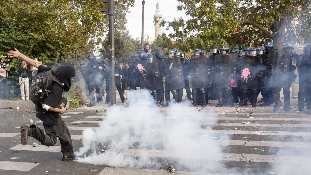 A protester kicks a tear gas canister as police watch on during disturbances in Paris on 6 October