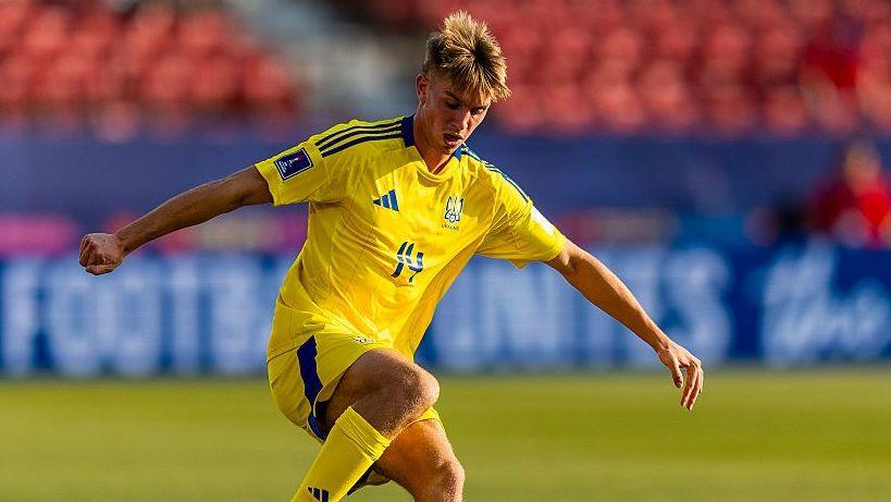 Kristian Shevchenko wears a yellow shirt and shorts of the Ukraine national team while playing for their under-20s side. He has his arms out wide while in action on the pitch during a match