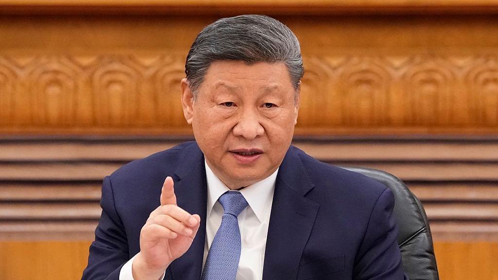 Chinese President Xi Jinping wears a dark blue suit and blue tie and is seen gesturing while talking