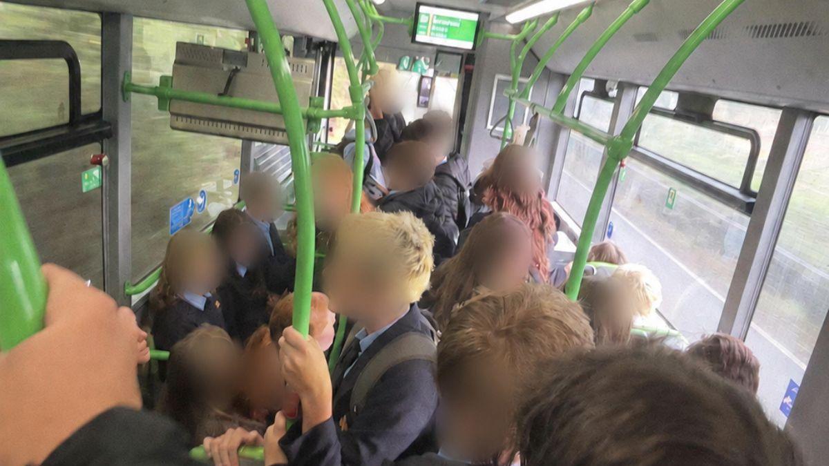 Pupils crowded on a Newport Bus service to Monmouth all wearing school uniform. They are standing in the aisle and holding on to the green handrails.
