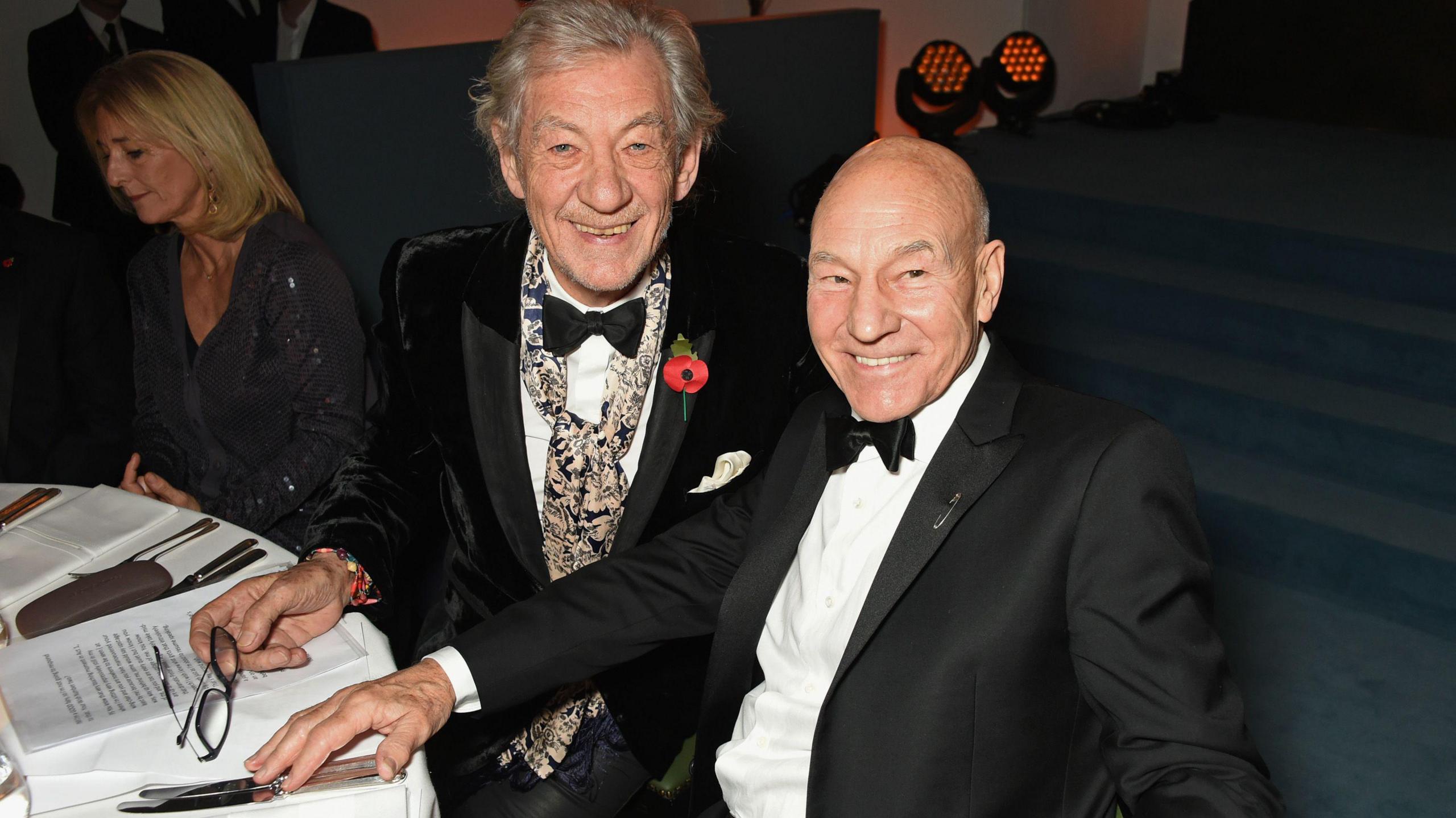 Sir Ian McKellen and Sir Patrick Stewart seated at a black tie event