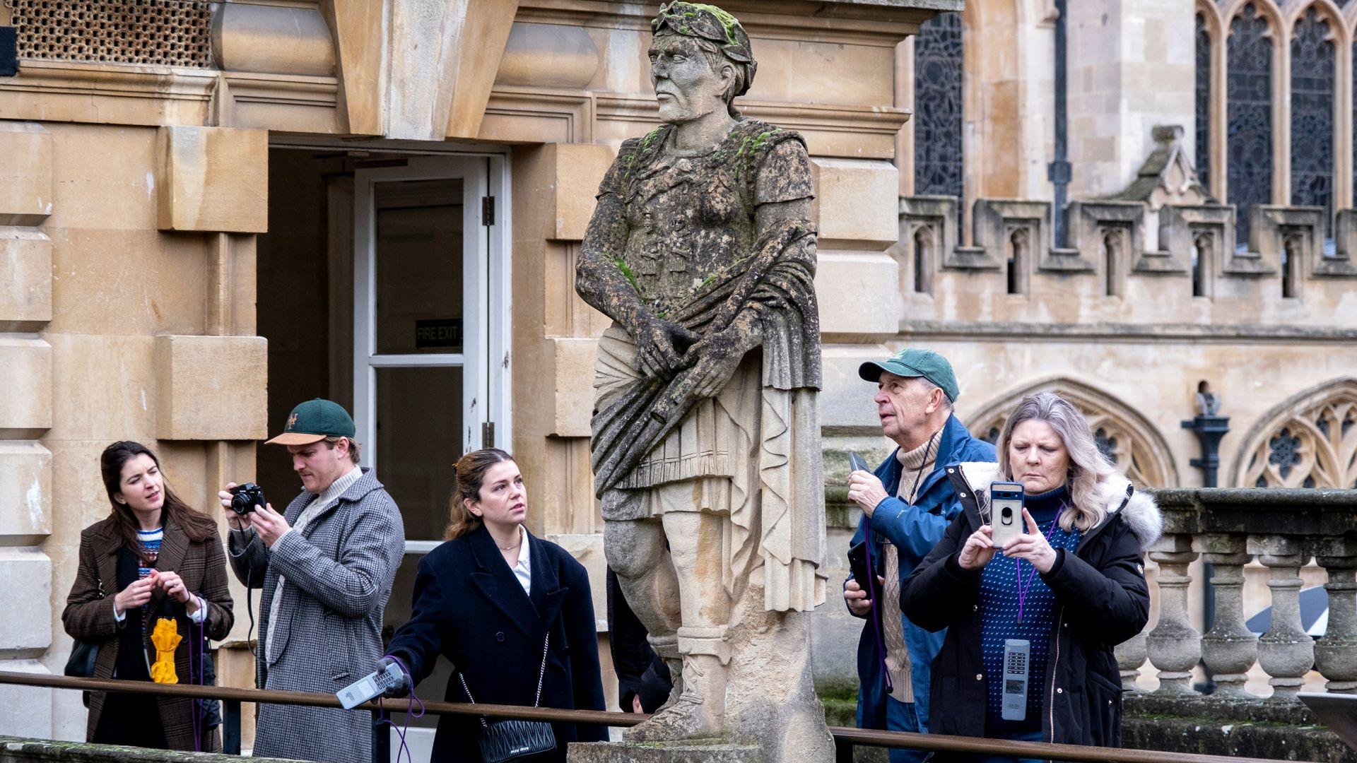 Tourists interact with Victorian statues of Roman Emperors on the terrace above the Great Bath at the Roman Baths on 27th December 2022 in Bath, United Kingdom