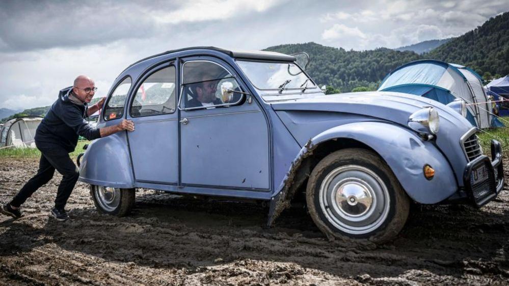 A man pushes a car out of the mud during the 24th World meeting of Citroen 2CV friends near Delemont, northern Switzerland on July 26, 2023.