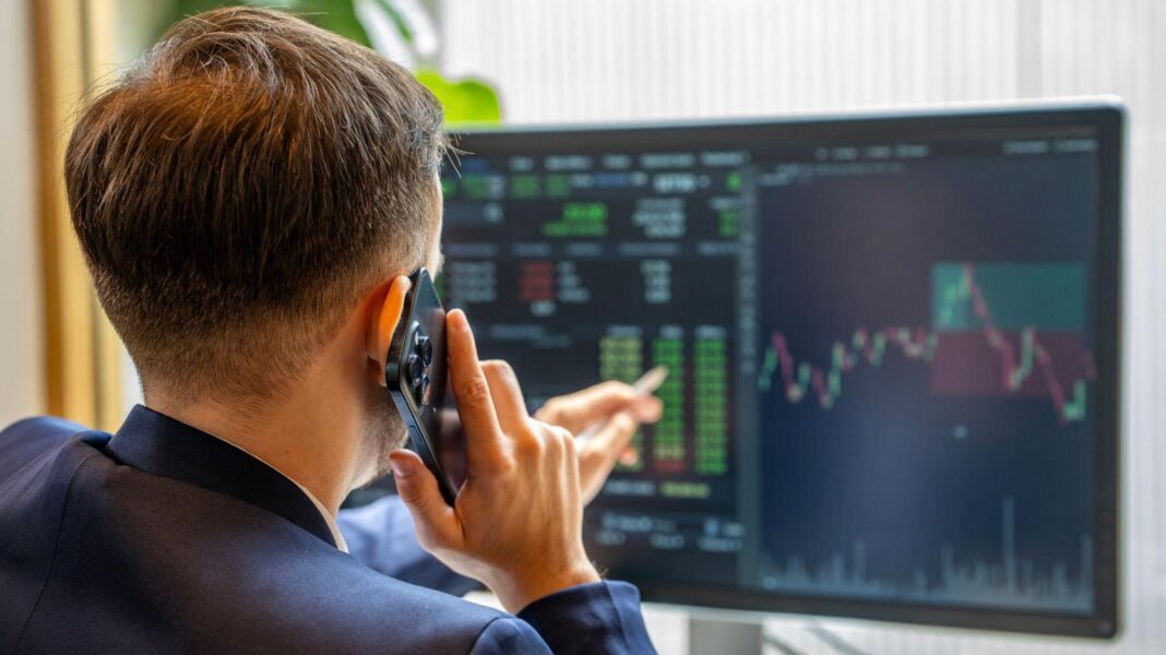 ‘Stop throwing shade’ – the woman trying to stop firms leaving the UK A man holds a mobile phone to his ear while pointing at a large computer screen that is displaying charts and numbers.