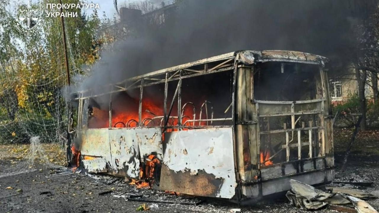 The burning metal shell of a bus in Kramatorsk. Flames can be seen inside the bus with black smoke coming out, with debris strewn across the road