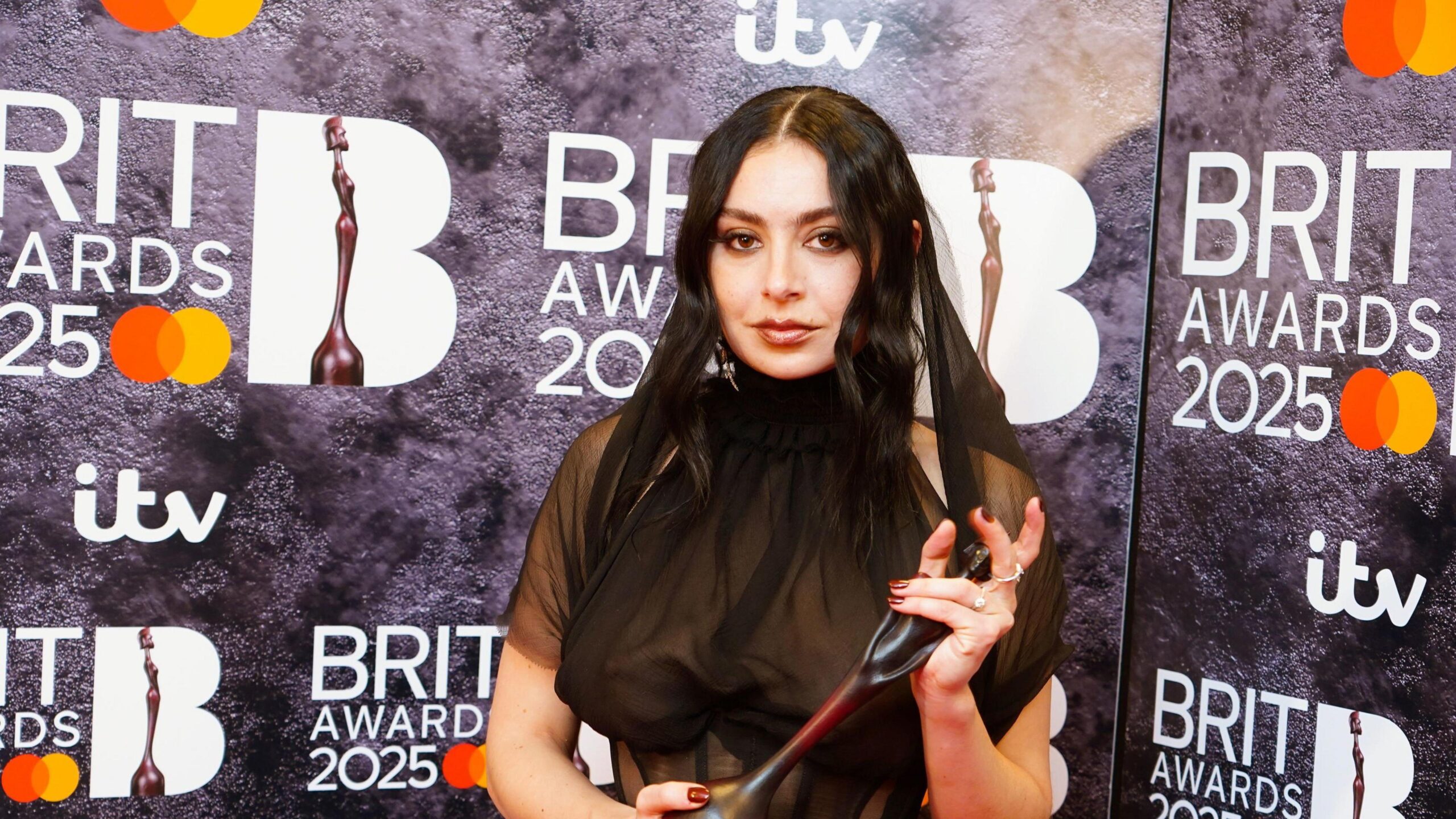 Charli XCX poses while holding an award in front of a backdrop saying Brit Awards 2025