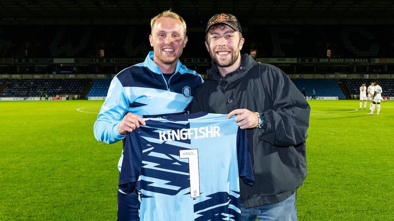 Two men holding a football top that says Kingfishr 1