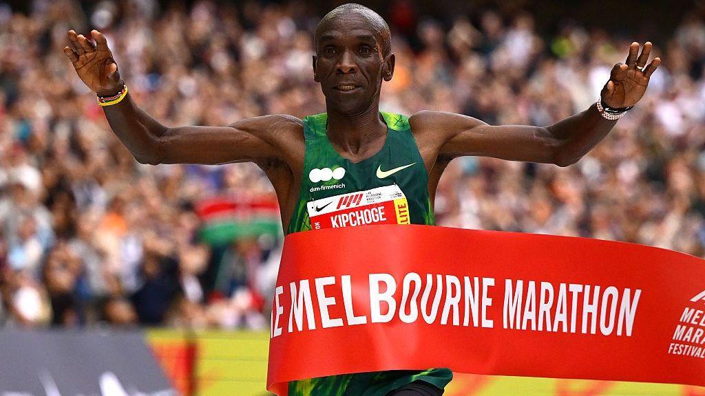 Eliud Kipchoge holding his arms aloft as he wins crosses the finish line.