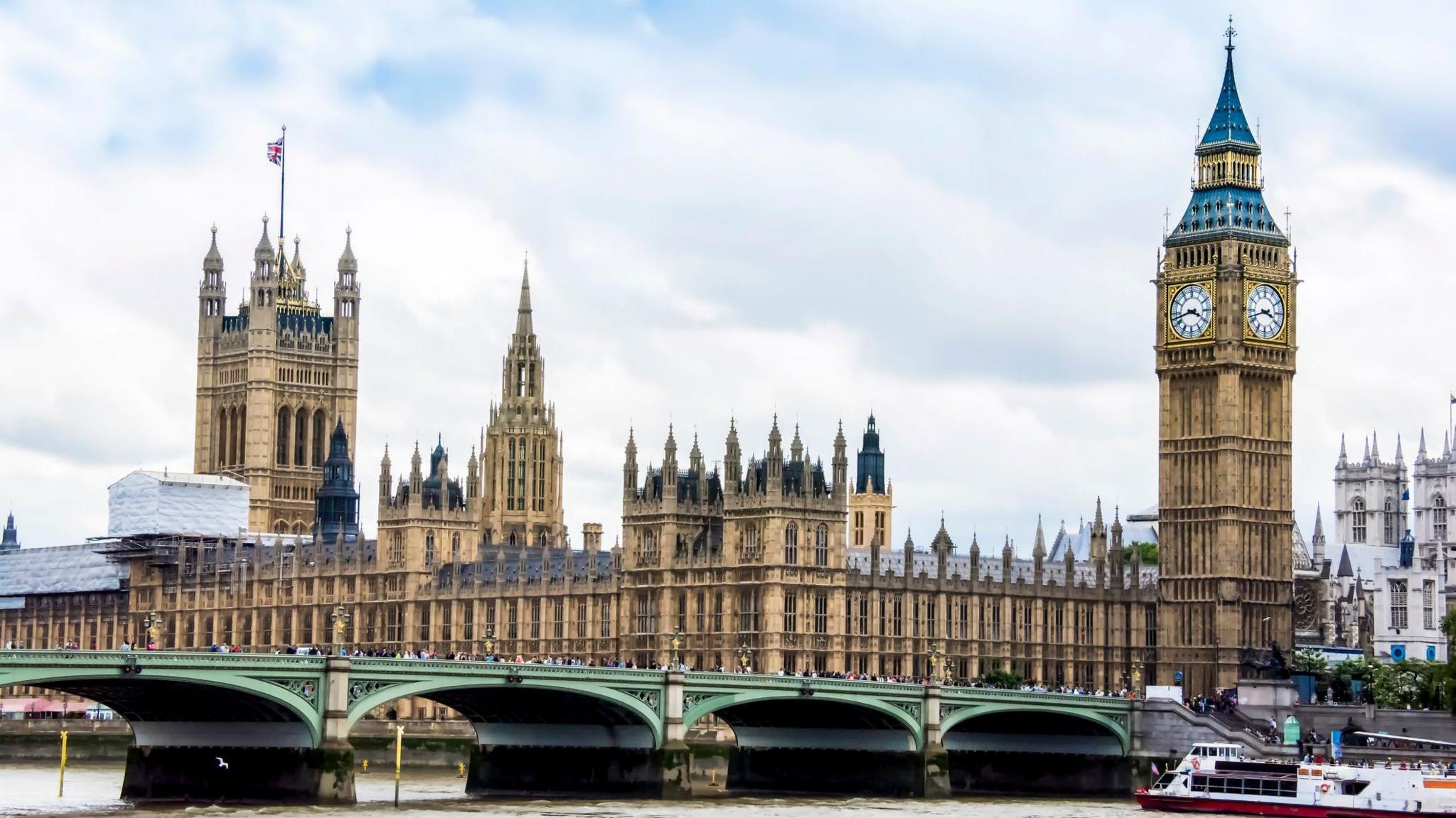 The houses of parliament. It is a yellow, gothic-looking ancient building. It sits by a river and bridge.