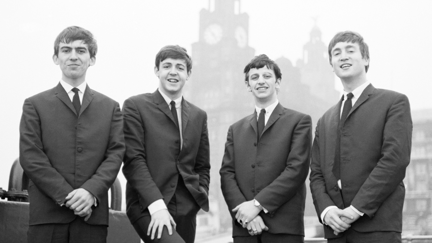 An early black and white photograph of The Beatles stood in front of the Liverpool Liver Building