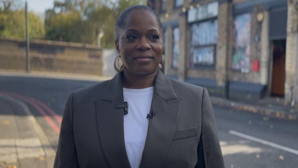 Charisse Beaumont, who is wearing a white T-shirt and a black blazer, stands outside a live music venue in Hackney.