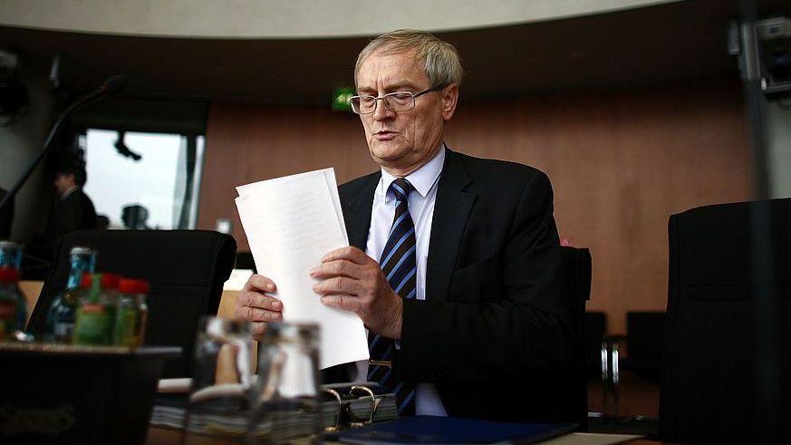File pic of a man called August Hanning from 2008, a man with grey hair and a dark suit and tie, holding papers as he sits at a desk