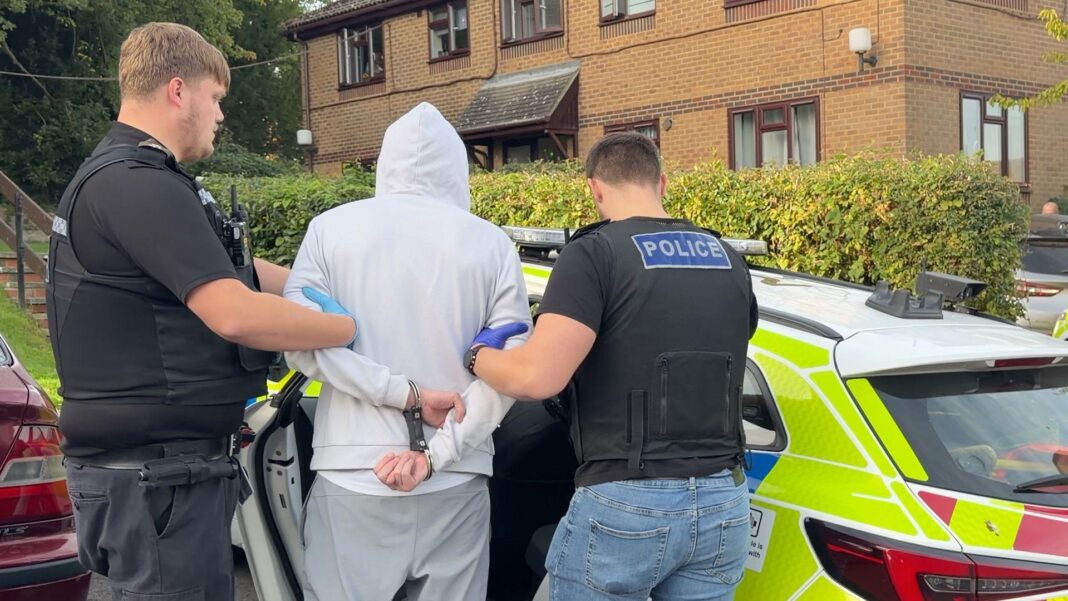 One stolen every four minutes – inside the police battle against vehicle thieves Police officers in plain clothes with police stab vests on top lead a handcuffed suspect wearing a hoodie into a police car, which is parked outside a low-rise, brick-built block of flats.