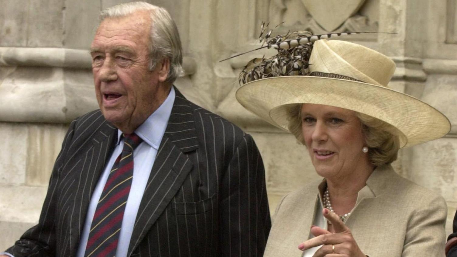 Queen Camilla in a hat beside her father Bruce Shand, wearing a suit and tie.