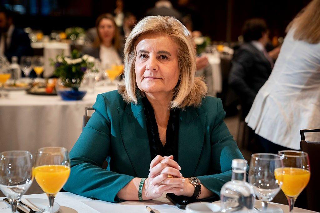 A woman sitting at a dinner table at an event. She has blonde shoulder length hair and a teal blazer on.