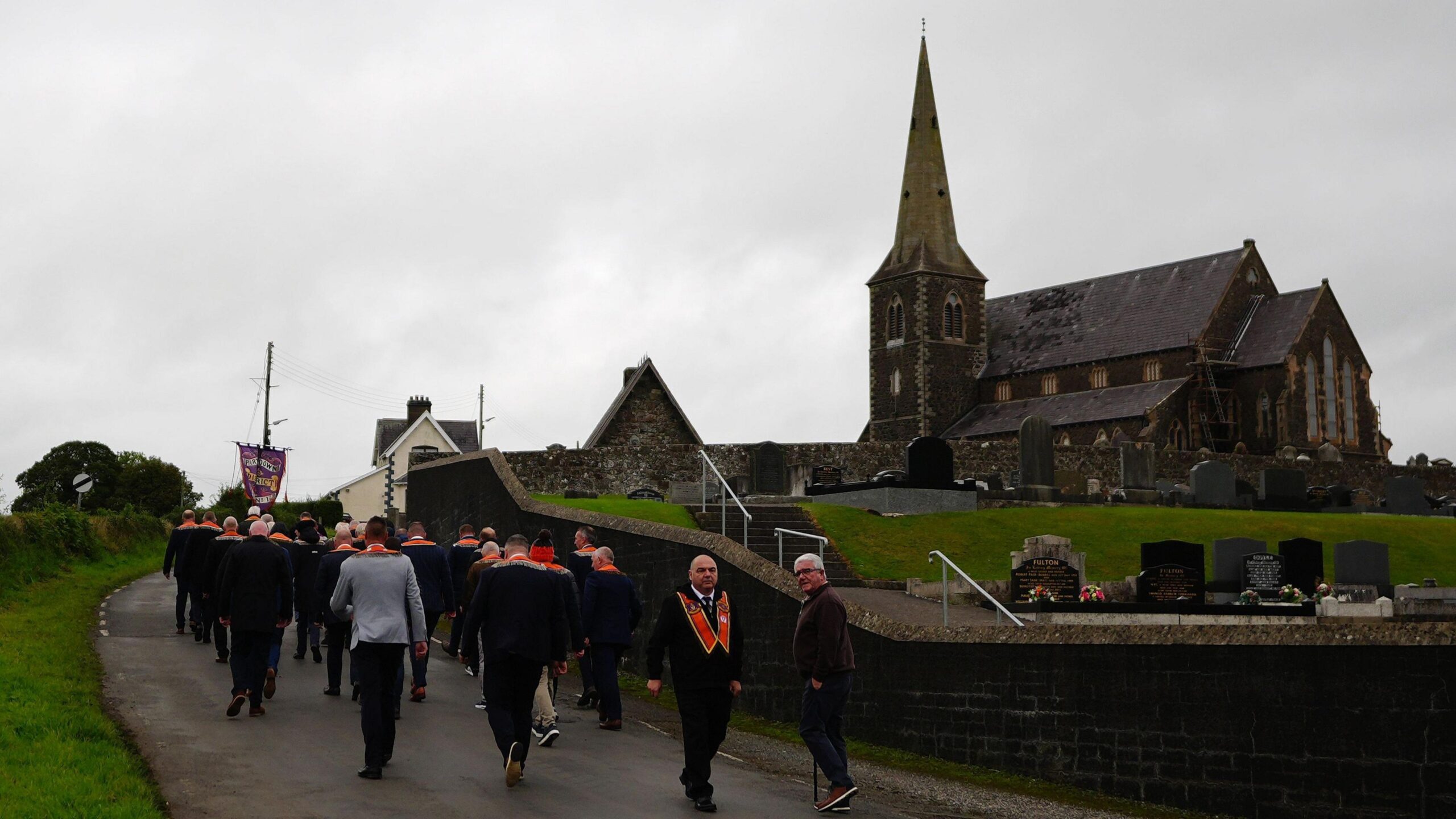 A group of Orangemen walking together, a church is in the background