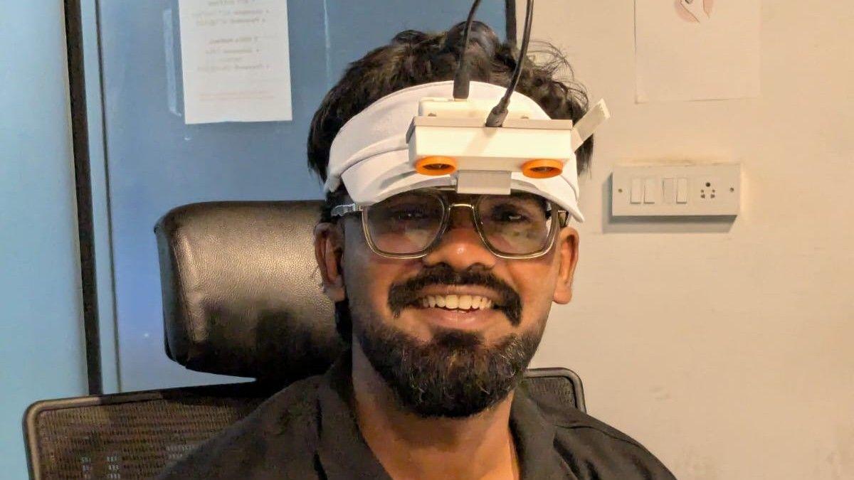 Shahil Baig wears white cap with a white camera attached. He's wearing glasses and smiling and looking at the camera.