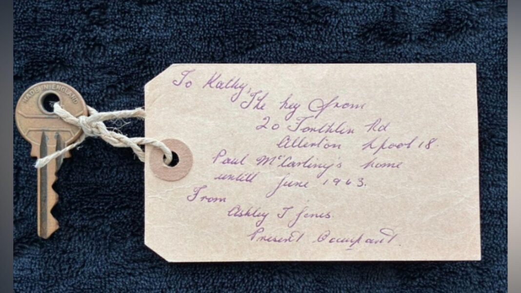 A silver house key with a paper label attached to it with string through the hole of the key. The paper label has old-fashioned handwriting on it which reads: 