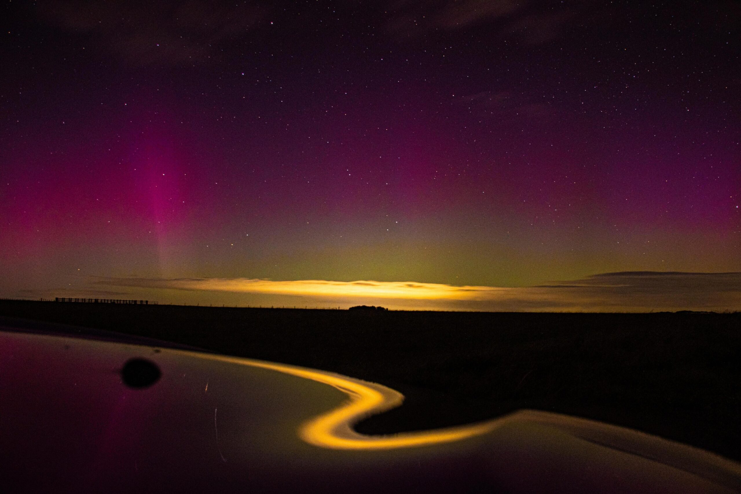 An image of the sky in Salisbury, Wiltshire, on 10 October during the evening. The Northern Lights can be seen in a pink hue above a bright horizon and what appears to be water reflecting the sky at the bottom of the image.