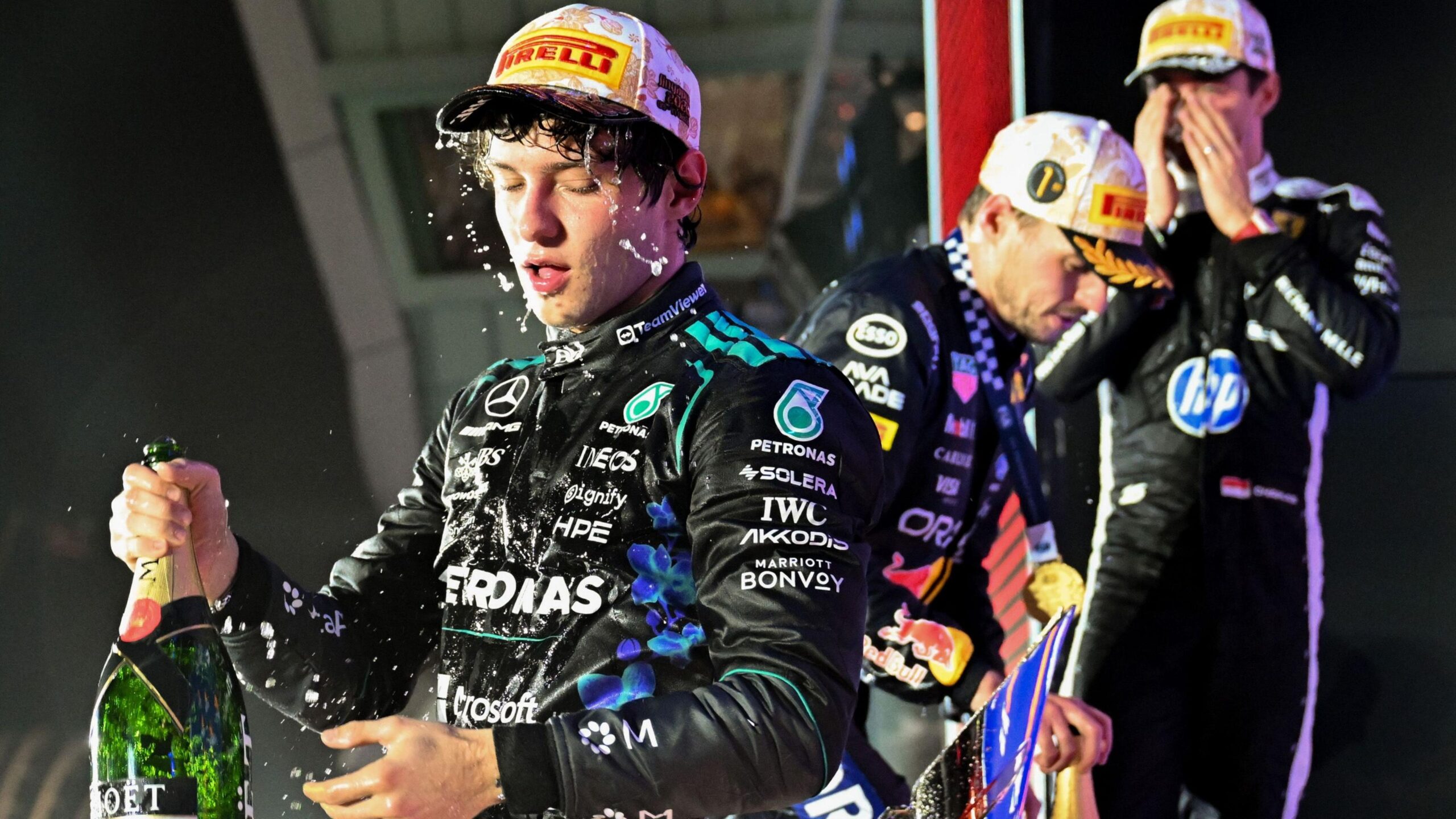 Mercedes driver Kimi Antonelli covered in champagne with Max Verstappen and Charles behind him on the podium after the Singapore Grand Prix