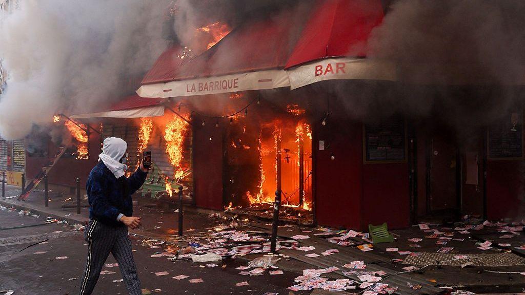 A man films as smoke rises from the bar 'La Barrique' on the sidelines of a demonstration against the "high cost of living", in Paris.