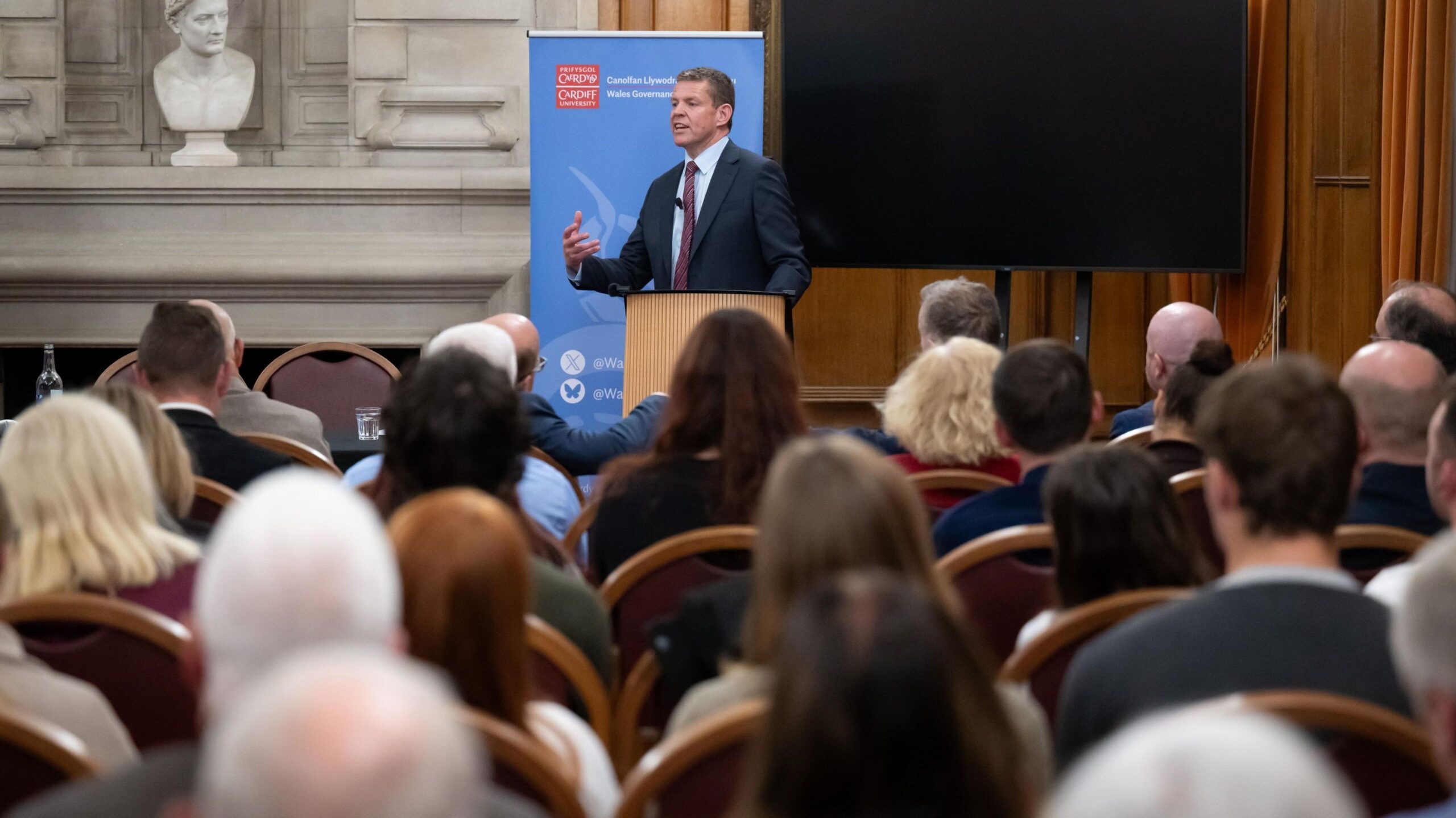 The first minister addressing a room of people in a lecture hall of Cardiff University