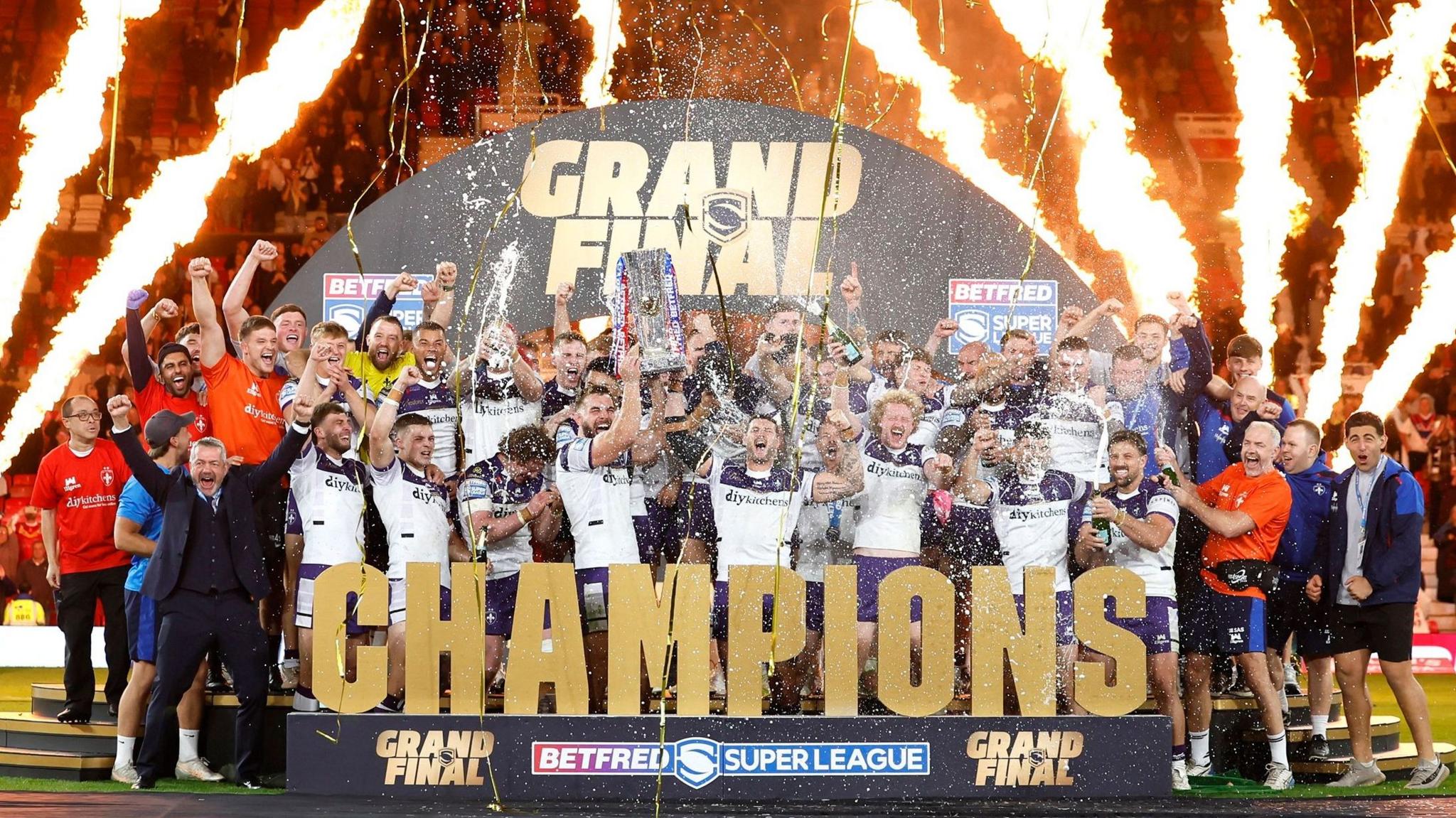 Wakefield Trinity hold the Super League trophy on a stage at Old Trafford with pyrotechnics going off in the background
