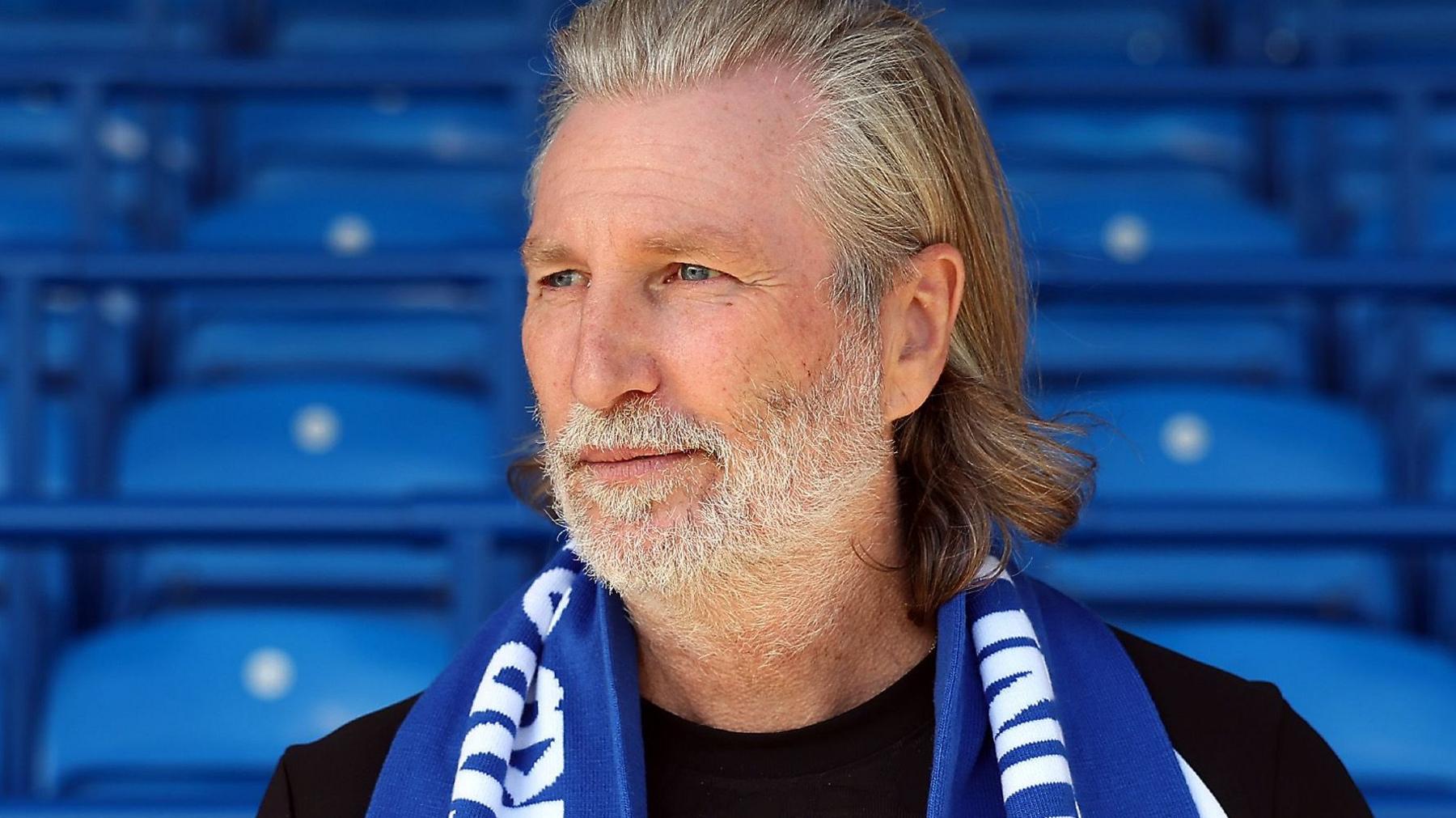 Robbie Savage in a black T-shirt poses with a blue Peterborough scarf.