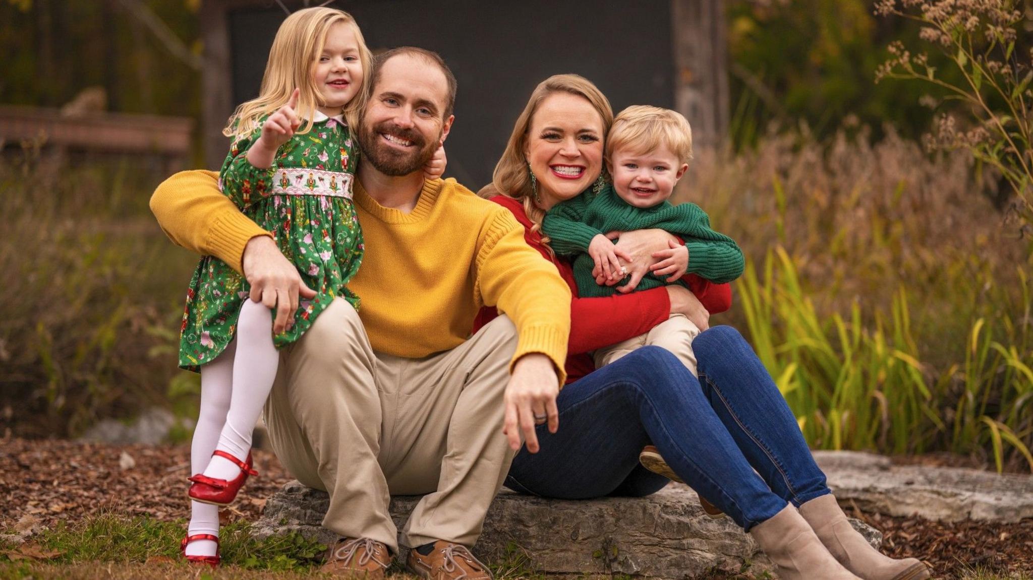 Wally Luckeydoo with his wife and two children. They are wearing bright clothing, and sat in a field