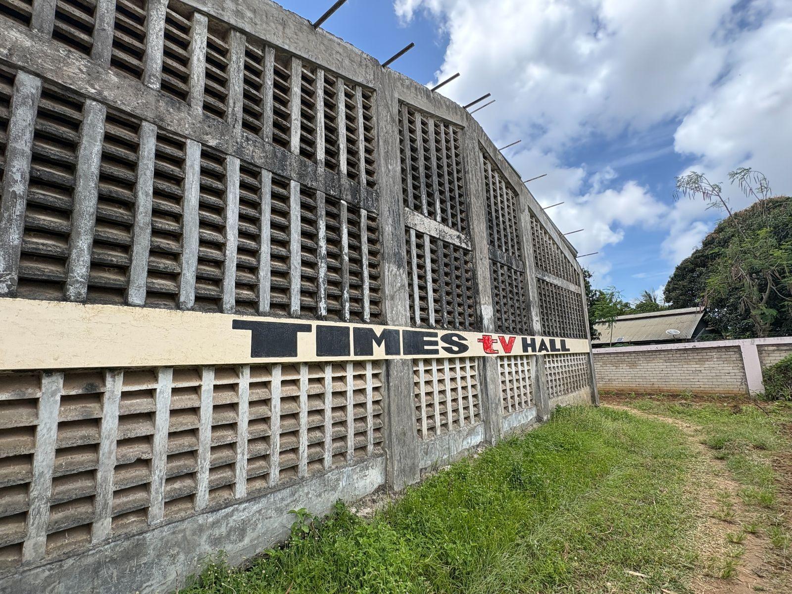 A grey concrete building with lots of air vents in the wall. There is a sign saying Times TV Hall