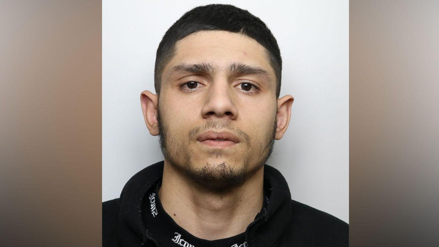A man with short cropped and dark eyes stares directly at the camera for a police mugshot.