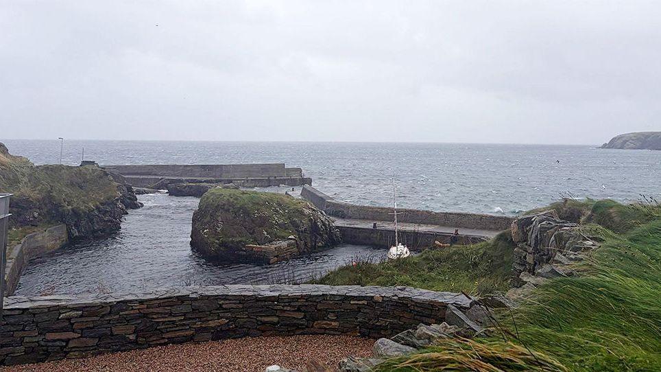 Port of Ness on the north coast of Lewis. There is a small boat sheltering in a harbour. The sky is  cloudy.
