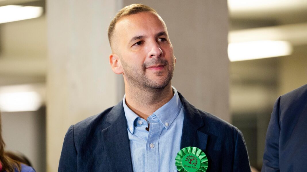 Mayor defects from Greens after Zionism motion Zack Polanski pictured wearing a blue shirt and blazer with a green 'Green Party' rosette on its lapel.