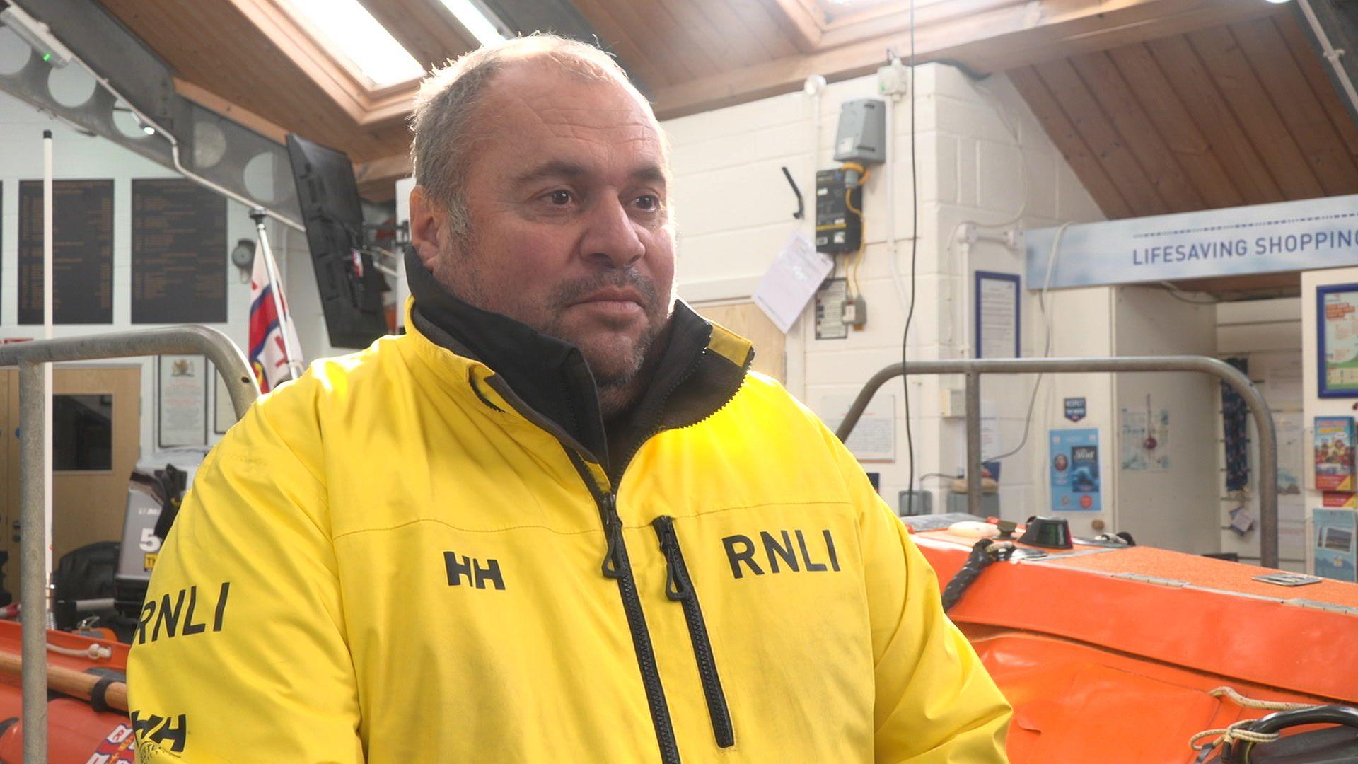 RNLI Coxswain Simon McCarthy is seen wearing a yellow RNLI coat inside the lifeboat station.