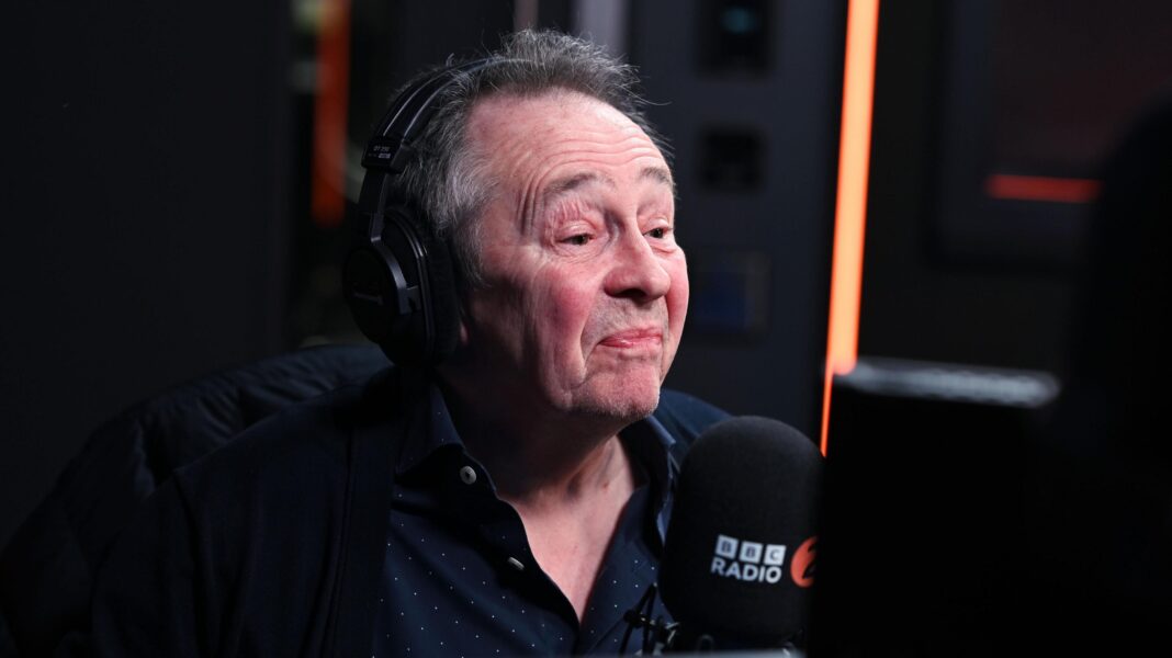 Comedian Paul Whitehouse mugged at London cash machine A man with grey hair and wearing a large set of headphones sits behind a BBC Radio 2 microphone.