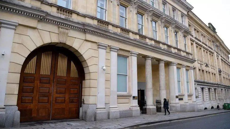 The exterior entrance of Bristol Crown Court. It is a large sand coloured building with white columns outside the front, and large arched wooden double doors on the left.