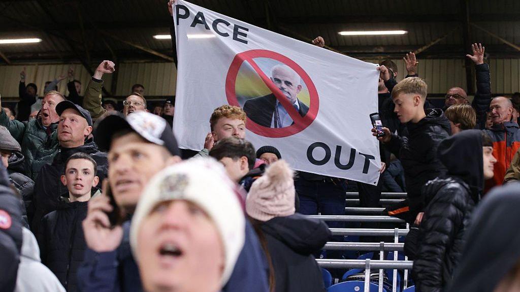 Burnley supporters display a banner depicting a photograph of owner Alan Pace with a red line through it and the words Pace Out