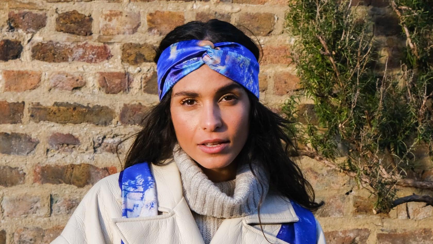 Chess Galea is looking straight at the camera wearing a blue scarf, and a beige coat and polo neck.