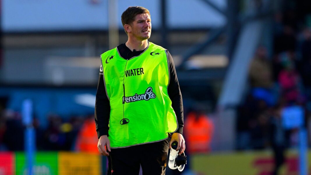Smith out injured as Saints make changes for Gloucester Owen Farrell of Saracens runs the water with a water bottle in his left hand while wearing a lime green fluorescent bib with the word "water" on it in capital letters.