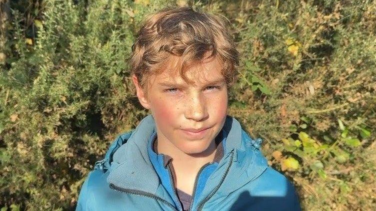 Liam has blonde curly hair and is smiling. He is wearing a blue jacket and blue fleece.