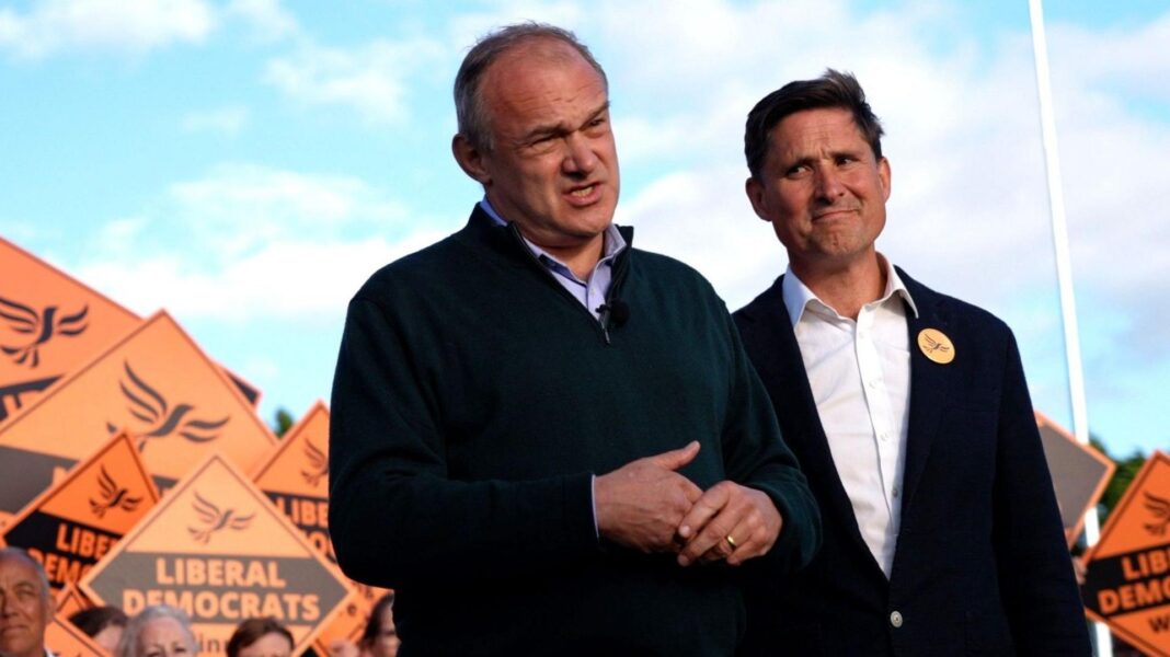Ed Davey standing next to Charlies Maynard in front of supporters holding several orange Lib Dem placards