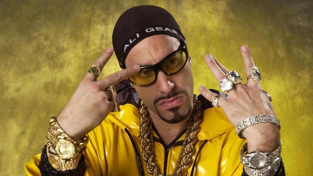 A man with loads of tacky jewellery, a yellow plastic suit and black beenie.