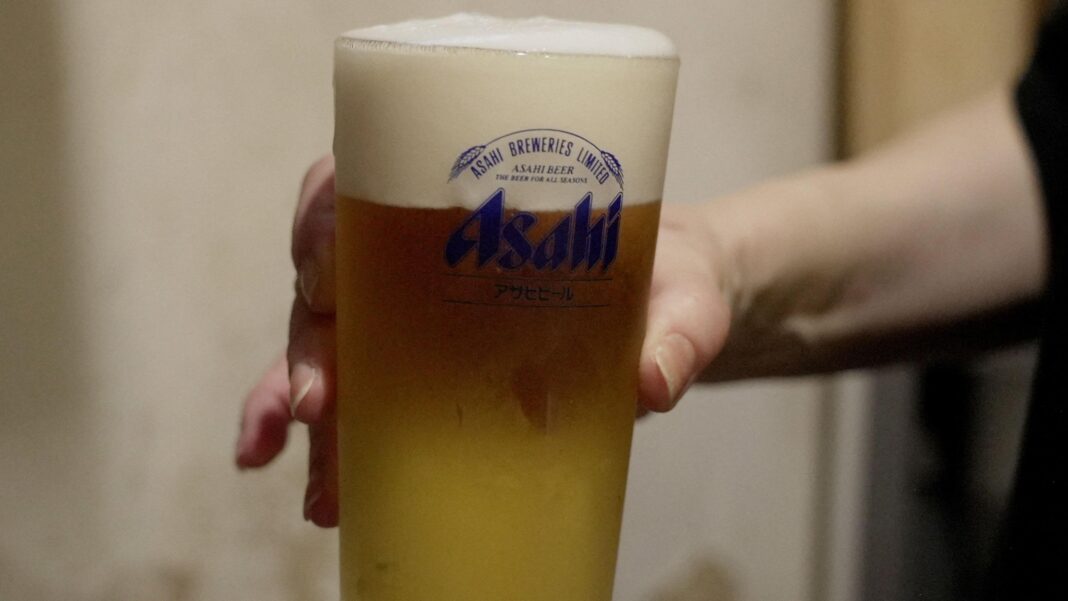 Japan beer giants raided over alleged price-fixing cartel A person holds a large glass of beer in their right hand with Asahi Breweries written on the glass in blue letters.