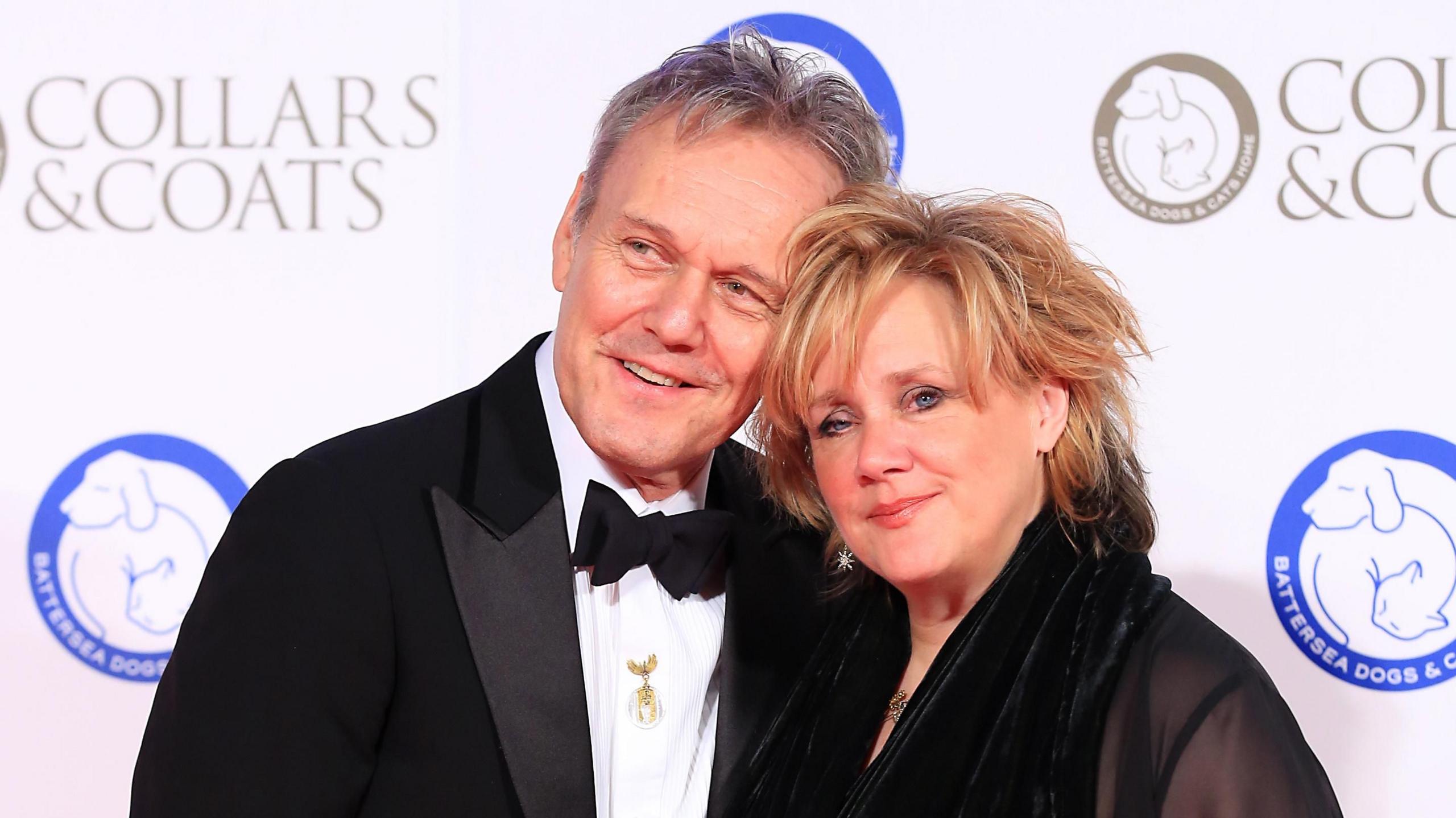Anthony Head and Sarah Fisher, a couple in their 60s at a red carpet premiere wearing formal attire