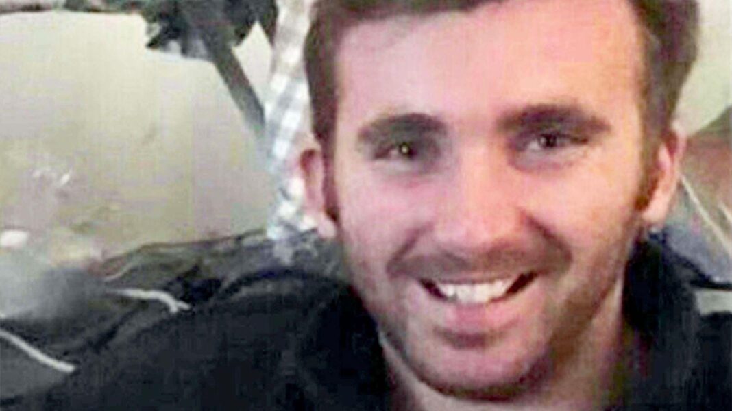 L/Cpl George Hooley smiling at the camera, he is a white man with dark hair and a beard.