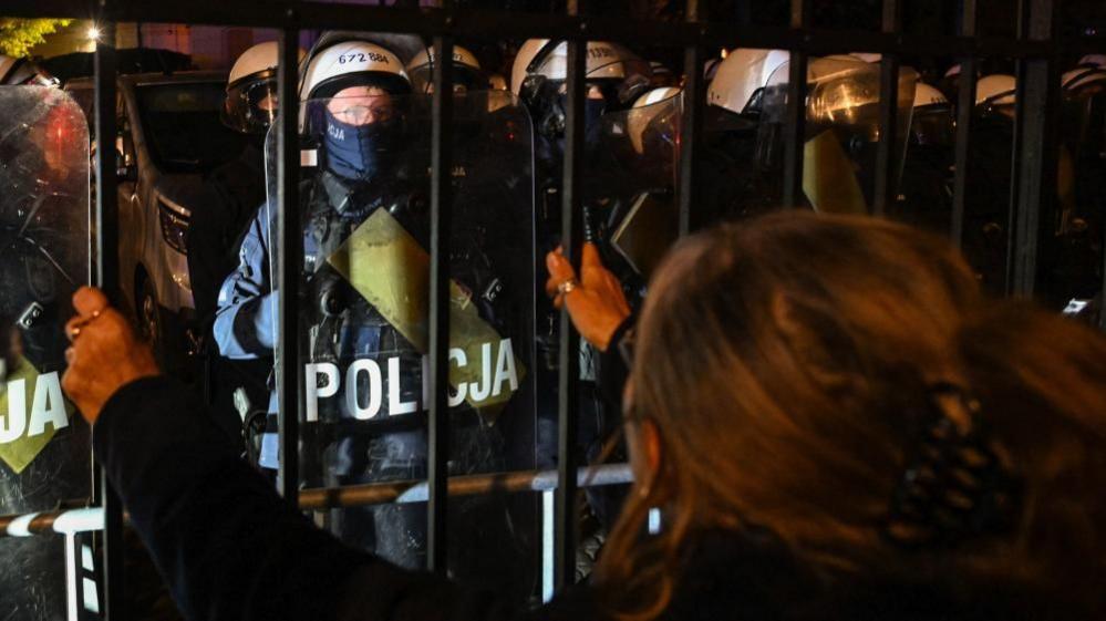 A woman looks at police officers standing guard outside Poland's Constitutional Tribunal in Warsaw. Photo: 30 October 2026