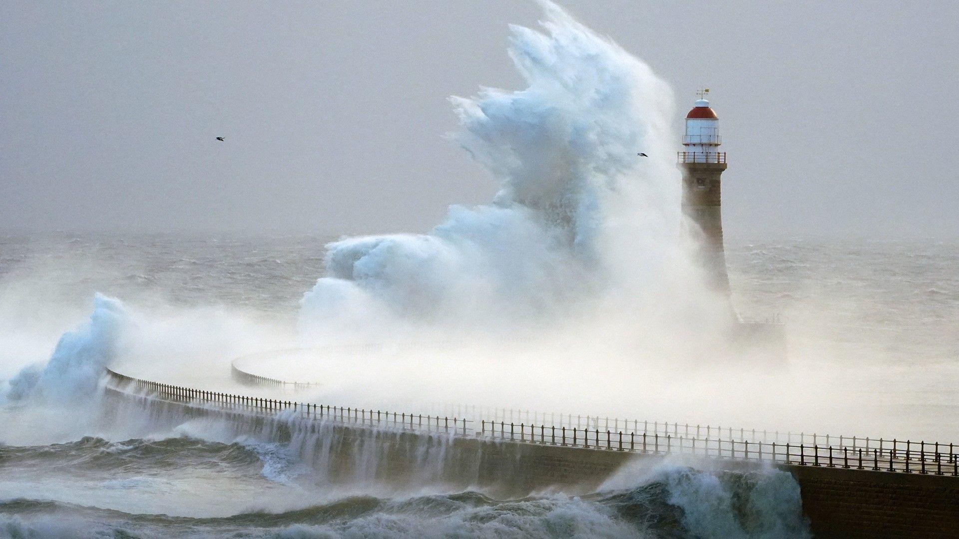 Lighthouse surrounded by rough seas during a cloudy and stormy day with large waves crashing over the structure.
