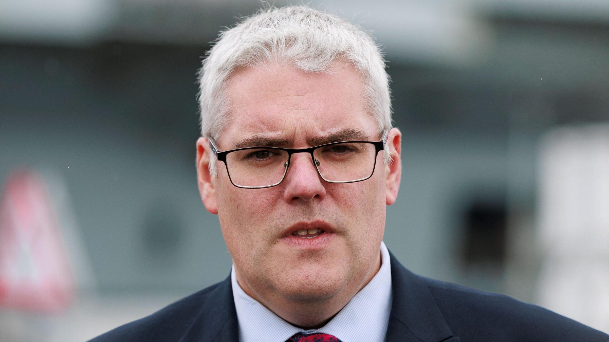 A man with white hair wearing glasses and a suit