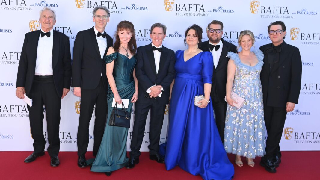 The cast of Gavin and Stacey, from left to right: Larry Lamb in a black suit with white shirt, next to him is Robert Wilfort in a black suit, white shirt and black bow tie, next to him is Melanie Walters in a green dress, to her right is Rob Brydon, who is also in a black suit, white shirt and black bow tie. Next to him is Ruth Jones in a blue dress, and on her right is James Corden in a black suit, white shirt and black bow tie, next to him is Joanna Page in a light blue floral dress and on the far right is Matthew Horne in a black shirt, black jacket and black pants.